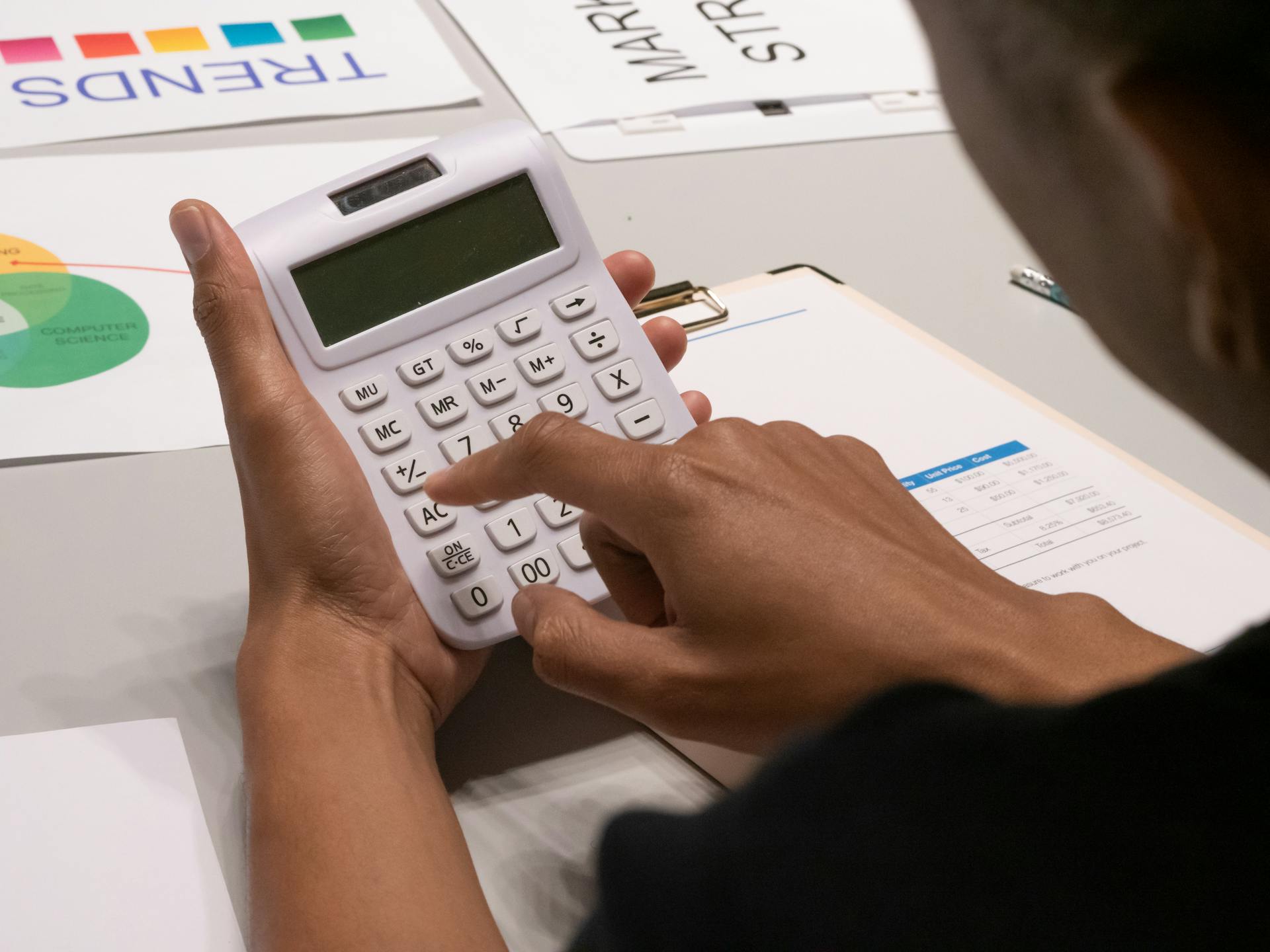 Focused image of a person using a calculator amidst financial documents and charts.