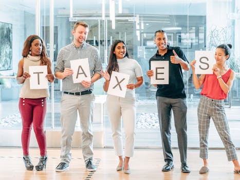 A diverse group of adults holding letters spelling 'taxes' in an office setting.
