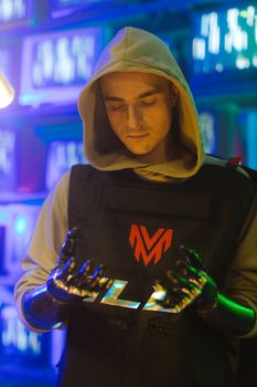 Man in hood with robotic hands in a cyberpunk setting with neon lighting.