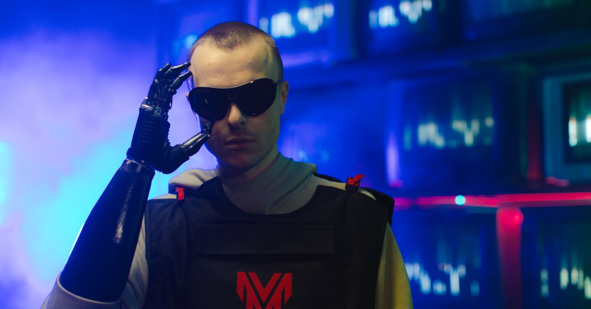 Portrait of an individual in futuristic gear, featuring a prosthetic arm and sunglasses.
