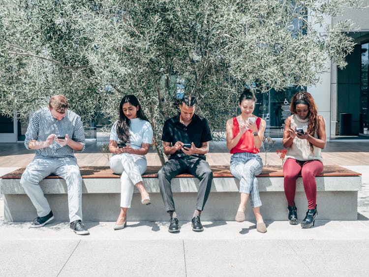 People Sitting On A Bench Using Smartphones