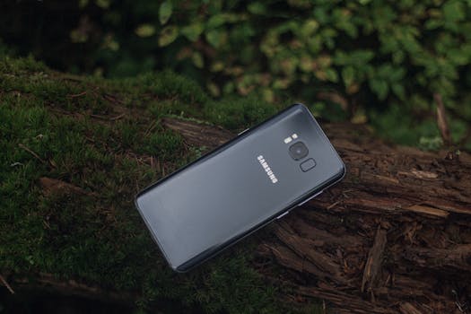 Close-up of a Samsung smartphone resting on tree bark with lush greenery.
