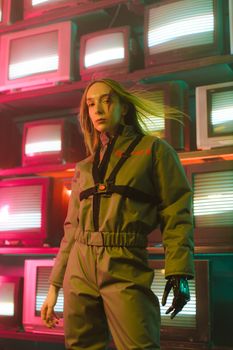 Futuristic portrait of a woman in a jumpsuit with prosthetic hand amid retro TV screens.