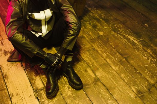 Man sitting on wooden floor with futuristic attire and prosthetic arm in cyberpunk setting.