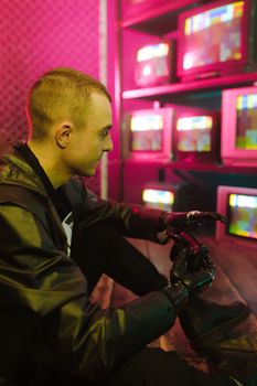 A man with a prosthetic arm sits in a cyberpunk environment illuminated by pink light.