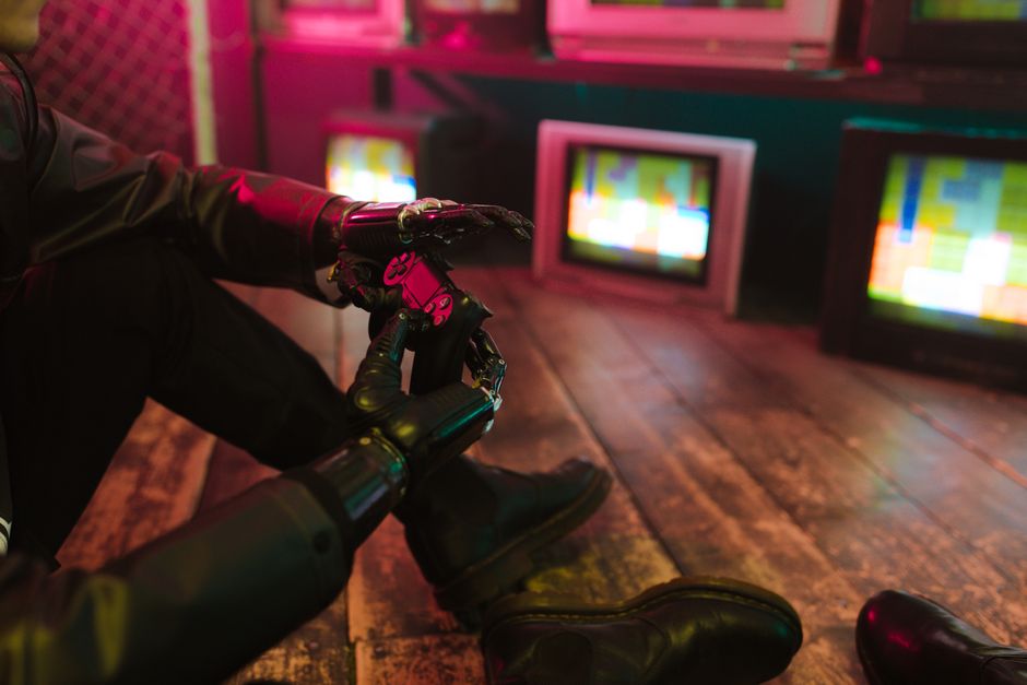 Futuristic cyberpunk vibe with a prosthetic hand holding a gaming joystick. Neon lights and retro TVs.