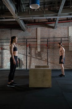 A man and woman preparing for a crossfit workout with box jumps in a spacious gym.