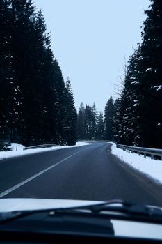 Scenic winter road through a snow-covered forest viewed from a car, showcasing tranquil travel.