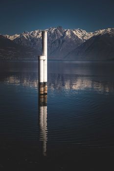 Scenery of peaceful dark blue water of lake and massive white metal pipes located in middle near snowy mountains under cloudless sky at sunset