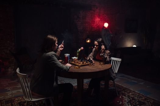 A couple engaged in a tense chess game indoors, amidst a moody and smoky ambience.