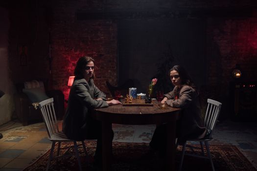 Two adults playing chess in a dimly lit room with a vintage vibe.