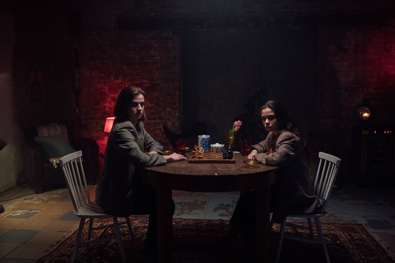 two adults playing chess in a dimly lit room with a vintage vibe