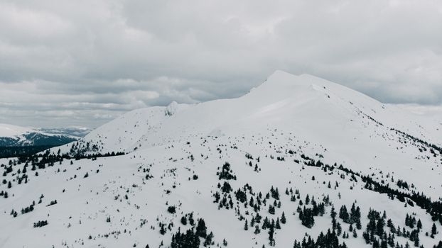 A stunning view of snow-covered mountains in Rakhivs'kyi district, Ukraine under a cloudy sky.