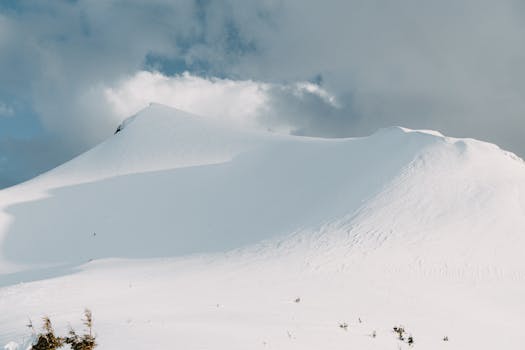 Scenic view of a snow-covered mountain peak under a cloudy winter sky, capturing nature's majestic beauty.