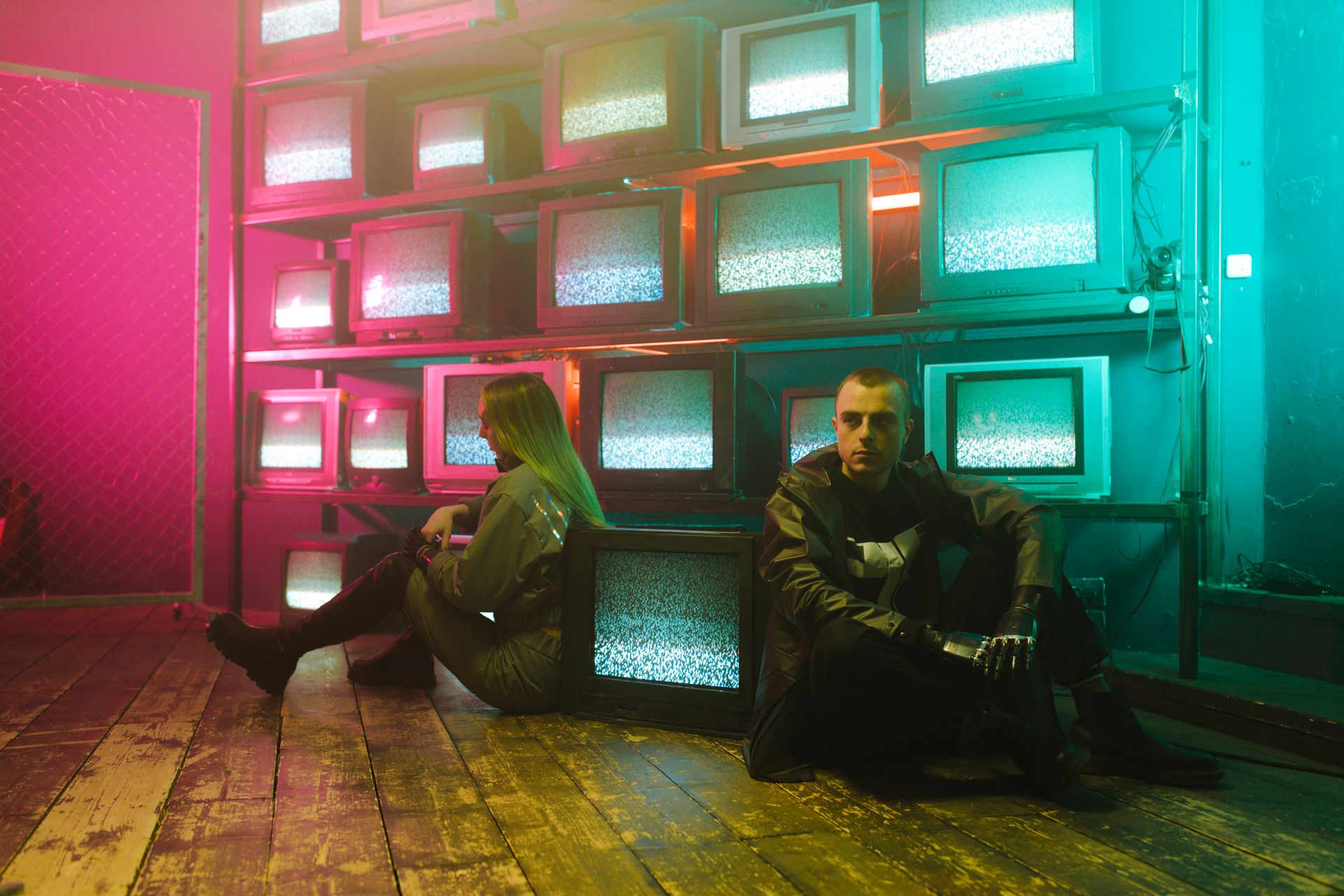 Man and Woman Sitting on the Floor beside Televisions