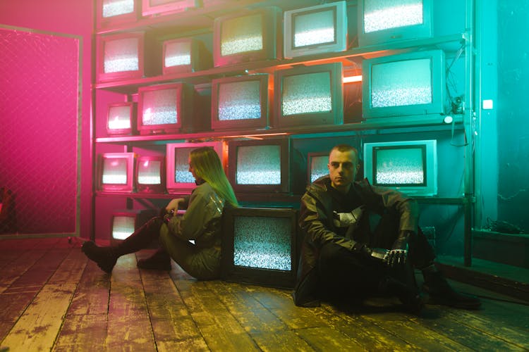 Man And Woman Sitting On The Floor Beside Televisions