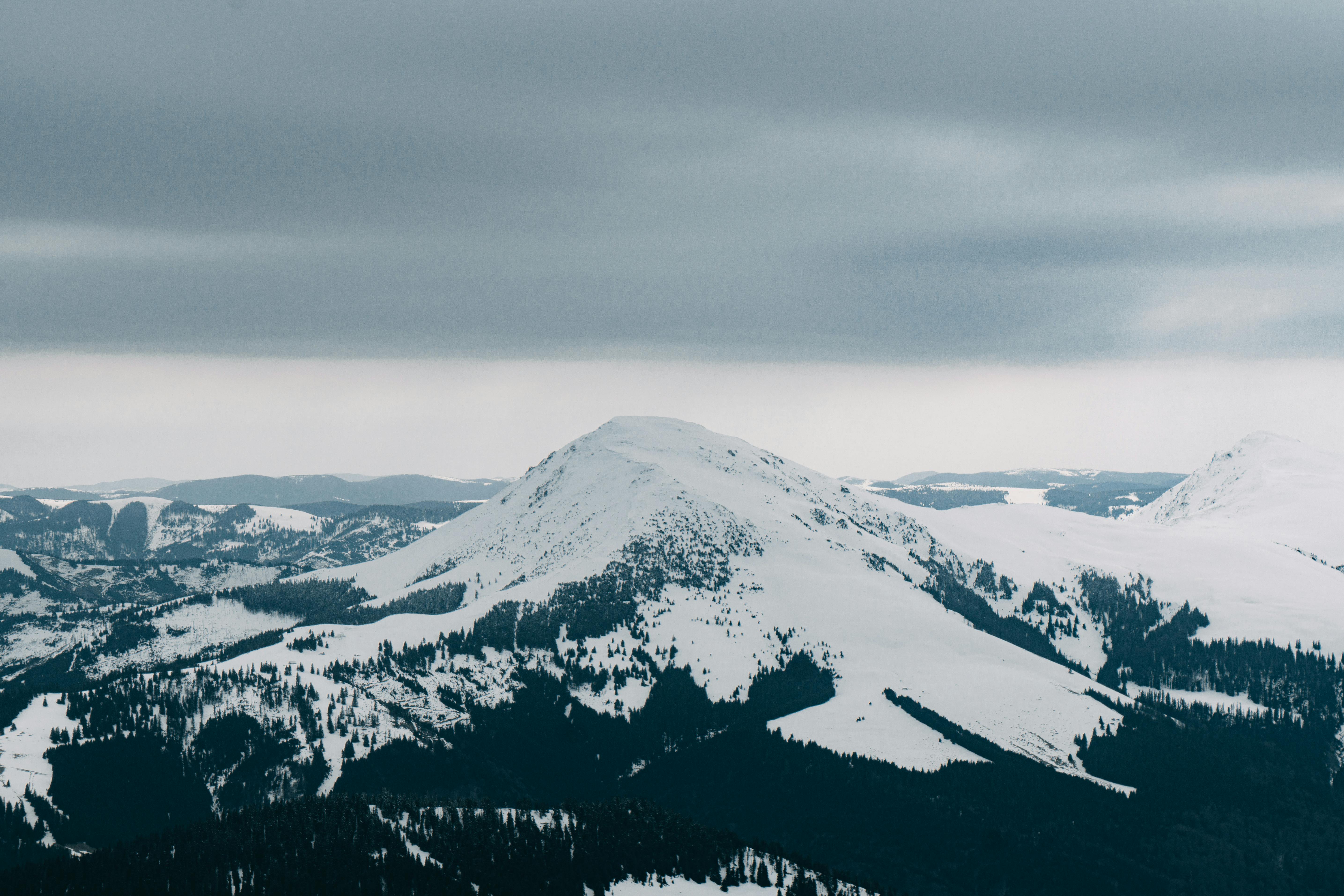 Breathtaking aerial view of a snow-covered mountain range under a moody winter sky, perfect for nature lovers.