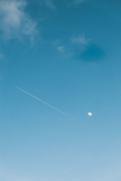 Free A serene sky photograph featuring a moon and airplane contrail against a clear blue backdrop. Stock Photo