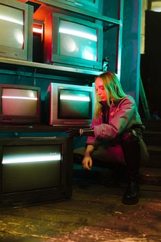 A woman with a prosthetic hand interacts with vintage televisions in a moody, neon-lit room.