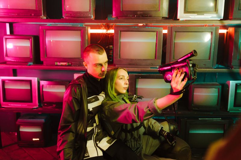 Futuristic cyberpunk couple taking a selfie with a retro TV backdrop and neon lights.