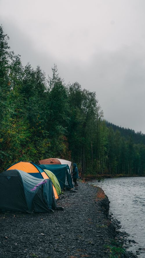 Free Vibrant tents set up by a tranquil riverside surrounded by lush forests. Stock Photo