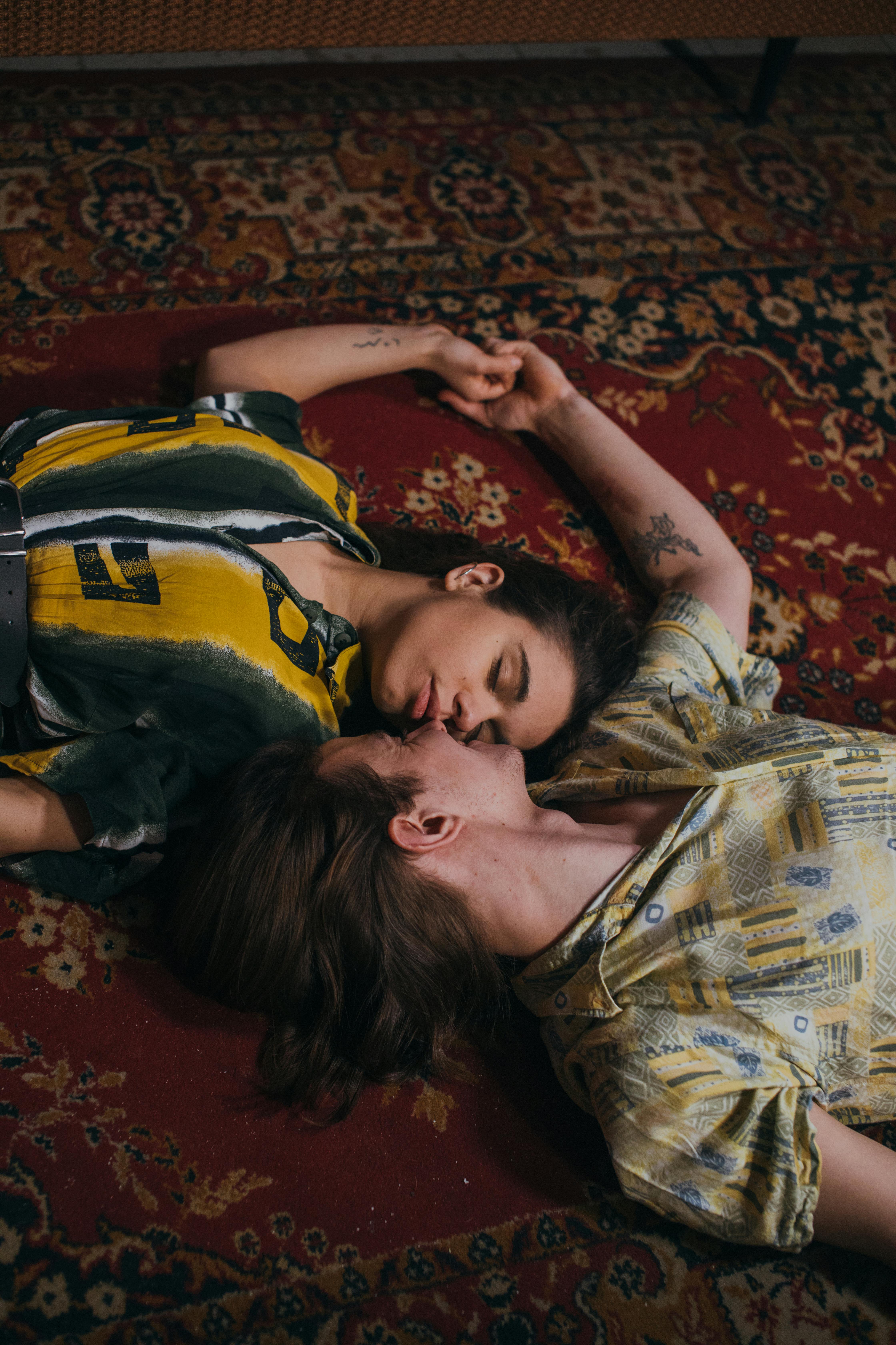 A loving couple lying on a vintage patterned rug, holding hands in an intimate setting.