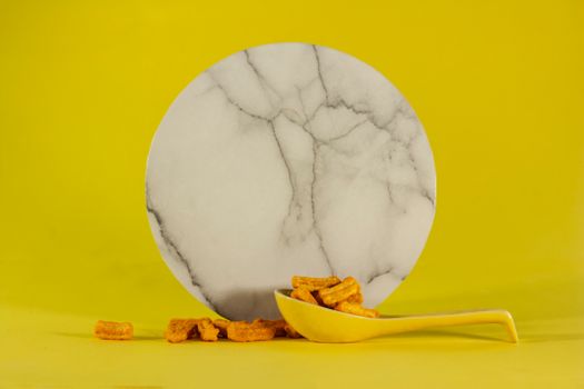 Minimalist marble plate with cornflakes on a yellow background, perfect for food and lifestyle imagery.
