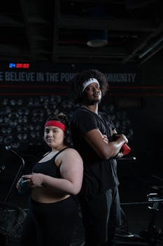 Two diverse individuals stand back to back in a gym promoting fitness and wellness.