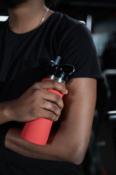 Close-up view of a man holding a red sports bottle, black shirt sleeves visible.