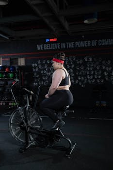 Plus size woman working out on an exercise bike in a gym, promoting body positivity and fitness.