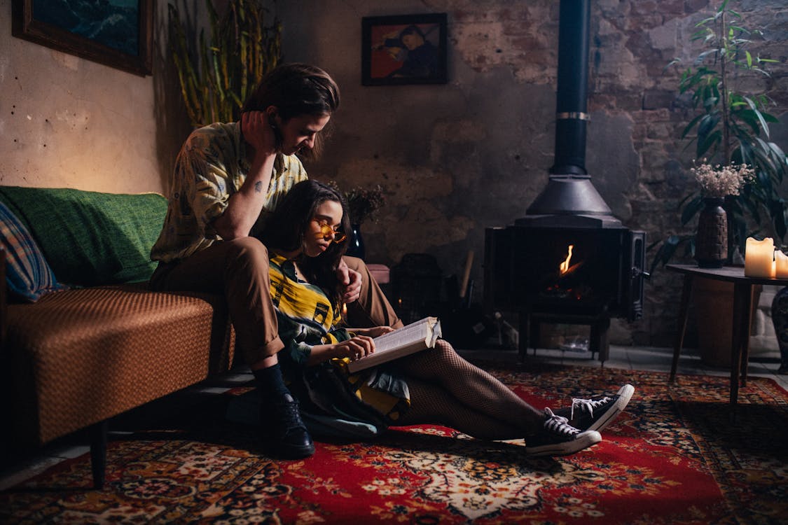 Free Woman Sitting on Floor Reading a Book with a Man Behind Her Stock Photo