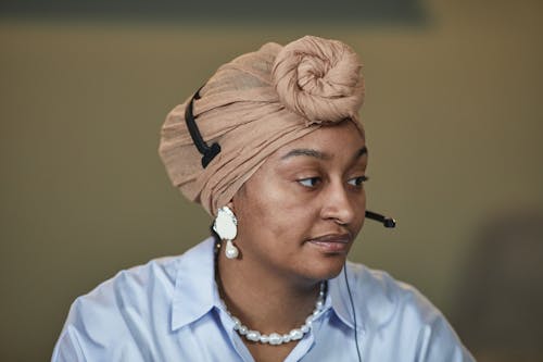 Woman in White Button Up Shirt and Brown Turban Wearing a Headset with Microphone