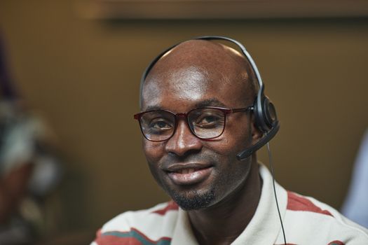 Portrait of a smiling man with a headset and glasses, indoors in an office setting.