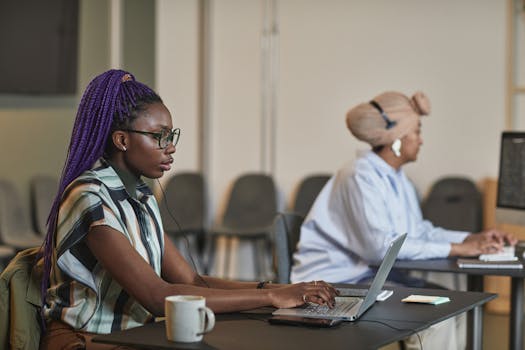 Two Black women working diligently at laptops in a modern office setting.