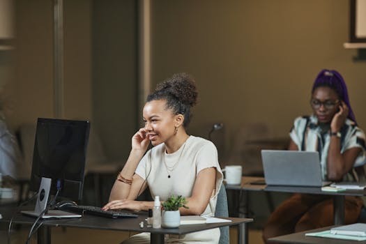 Two women engaged in work at a modern office, showcasing teamwork and concentration.