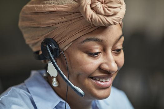 Close-up of a smiling woman in a headscarf with a headset, working in a call center.