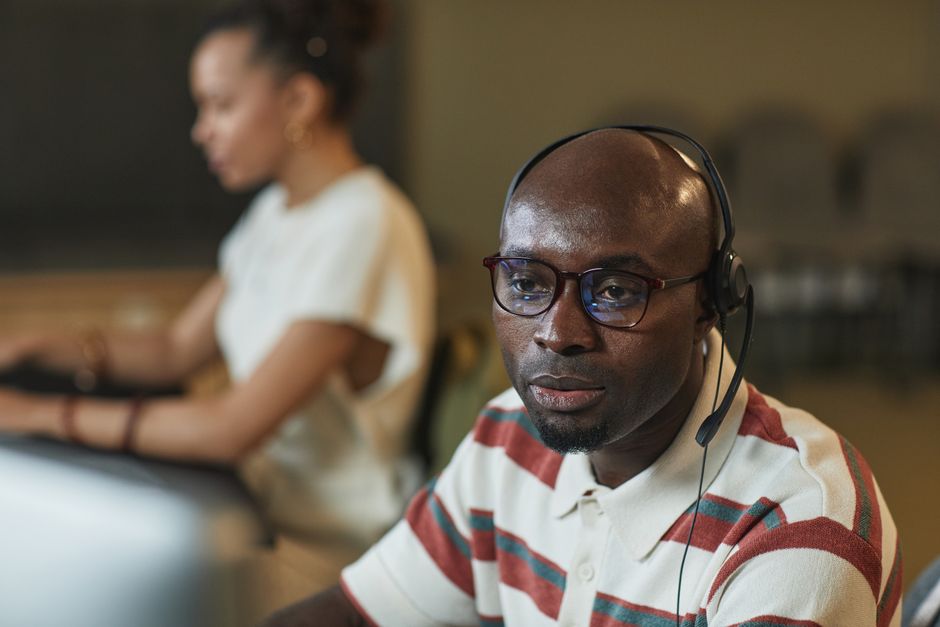 A man and woman working at a call center, wearing headsets with microphones.
