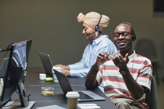 Two call center employees filing nails and working at desks with laptops and headsets in a casual office setting.
