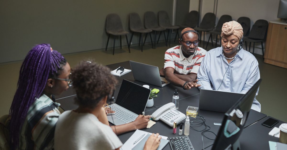 A group of diverse people working on a community science project with laptops and test tubes in a community center