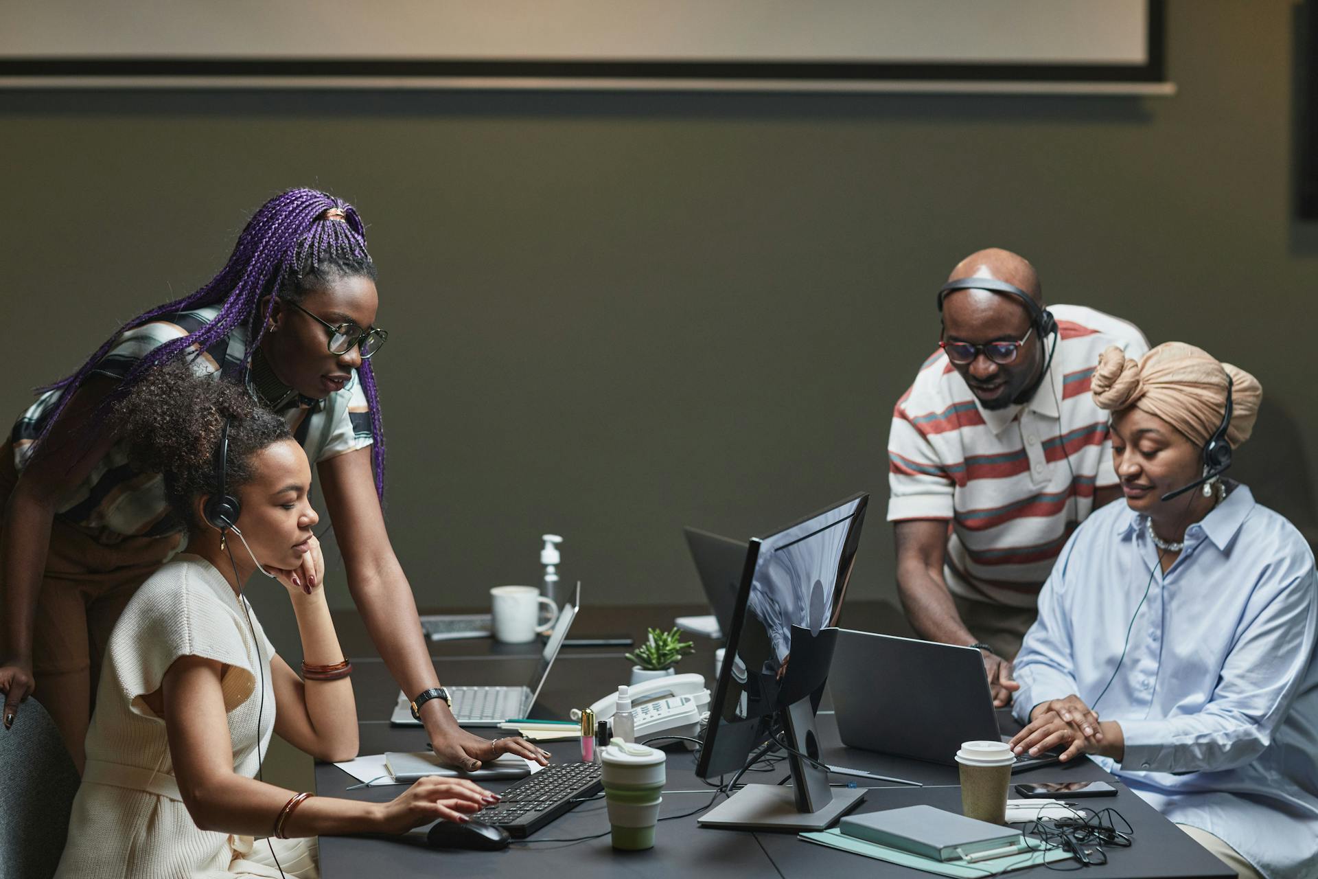 A diverse team of professionals collaborating in a modern office environment, using headsets and computers.