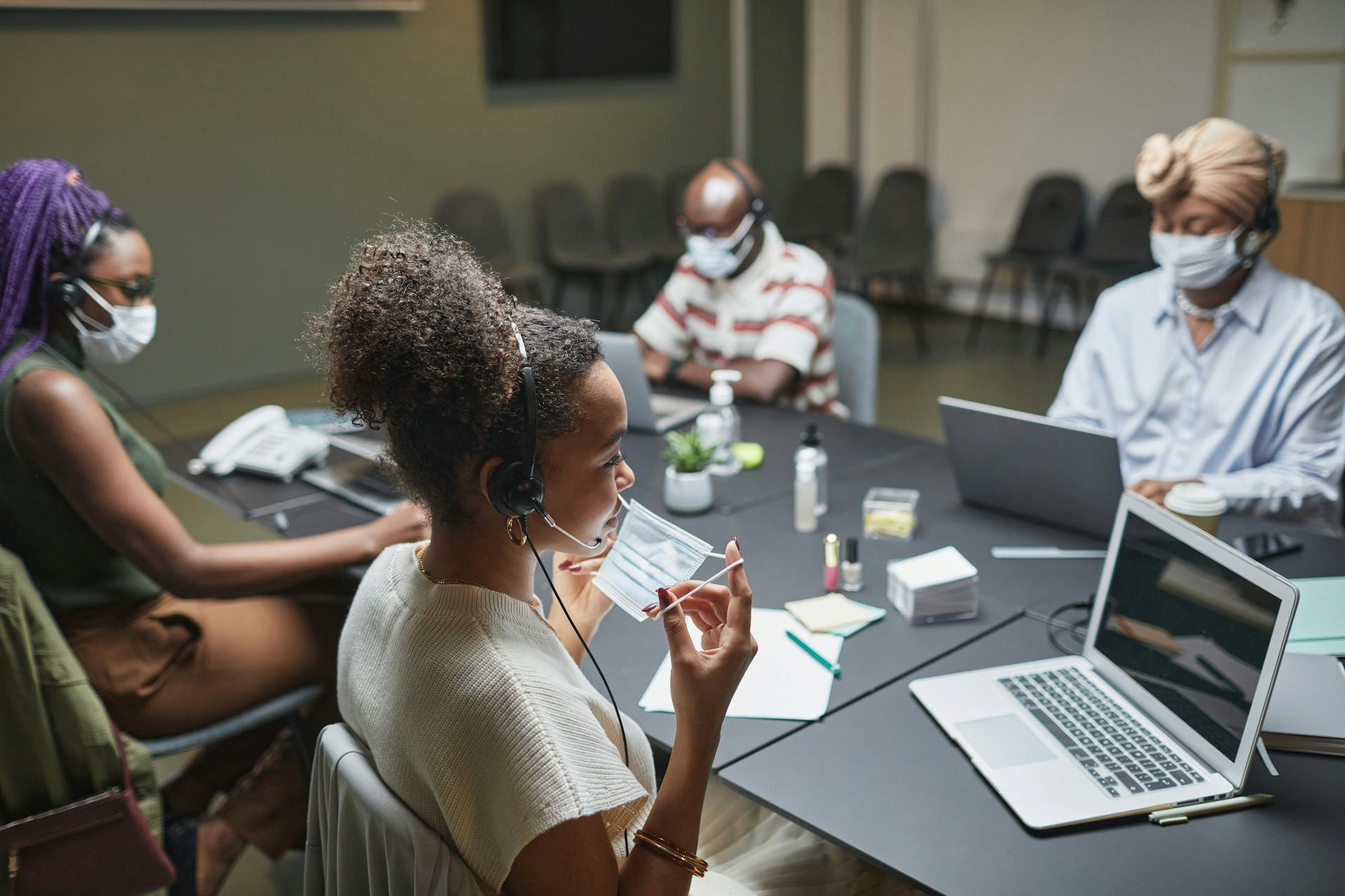 Colleagues collaborate in an office, wearing masks and headsets for safe teamwork.