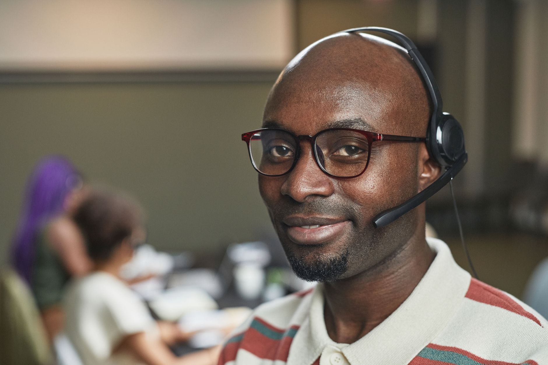 Smiling customer support agent wearing headset in a modern office setting.