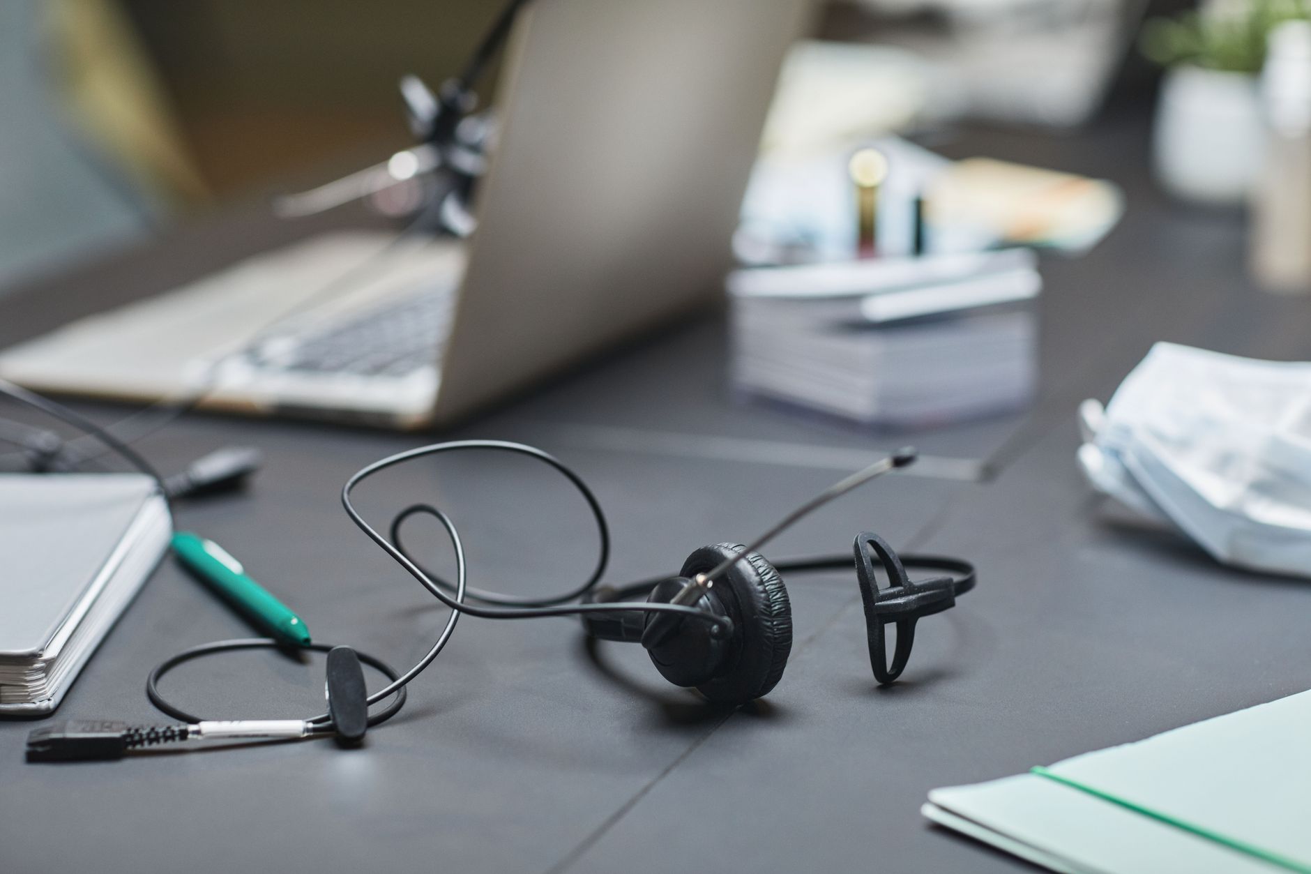 A close-up of office desk featuring a laptop, headset, and stationery, ideal for business settings.