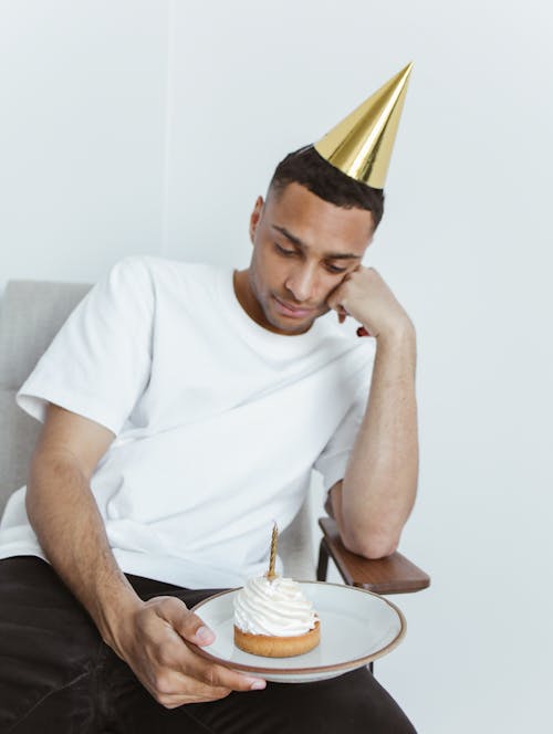 A Man Wearing Party Hat Looking the Cupcake