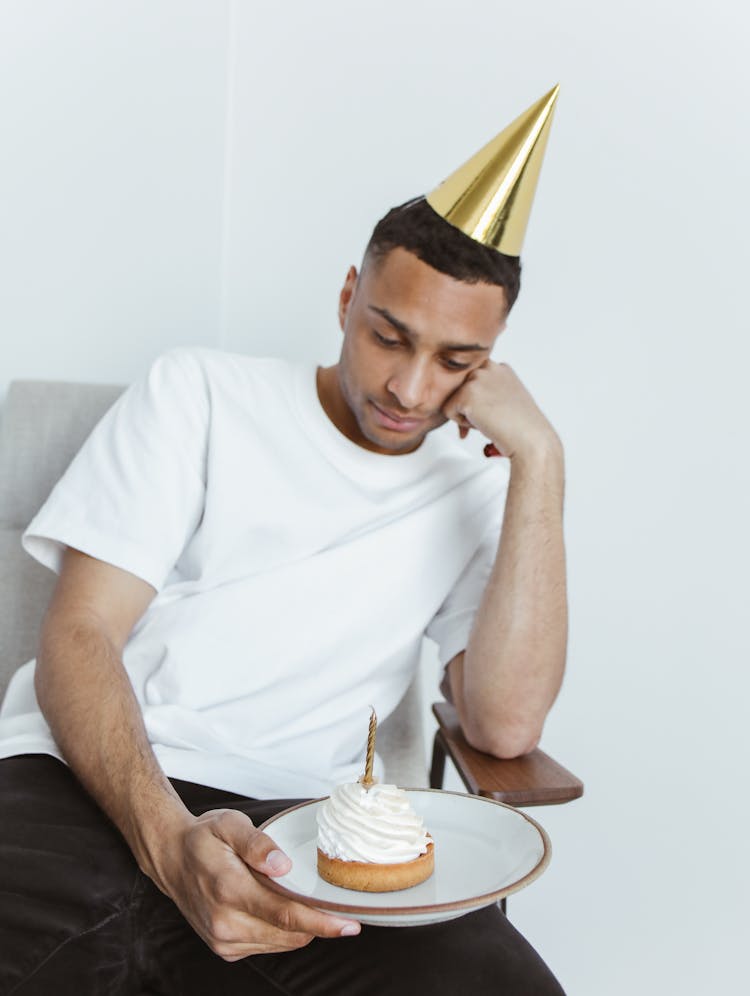 A Man Wearing Party Hat Looking The Cupcake