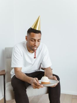 Young man in white t-shirt celebrates birthday alone with a cake.