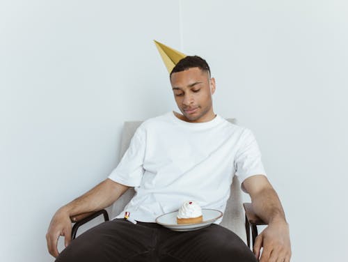 Man in White Crew Neck T-shirt and Party Hat Celebrating Alone