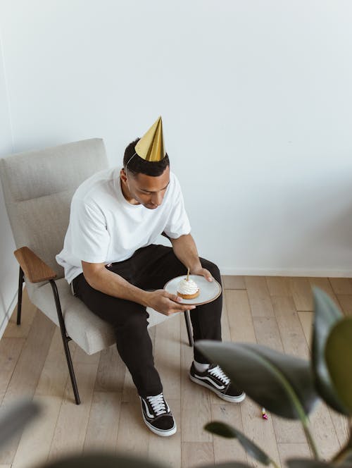 Man in White Crew Neck T-shirt and Black Pants Sitting on Gray Chair Celebrating Alone