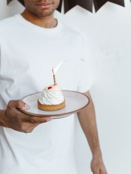 African American man holds a dessert with a birthday candle lit on a plate, ideal for celebration concepts.