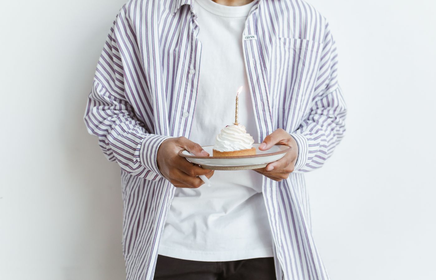 Person holding a cupcake with a lit candle, wearing a striped shirt. Celebrate special moments.